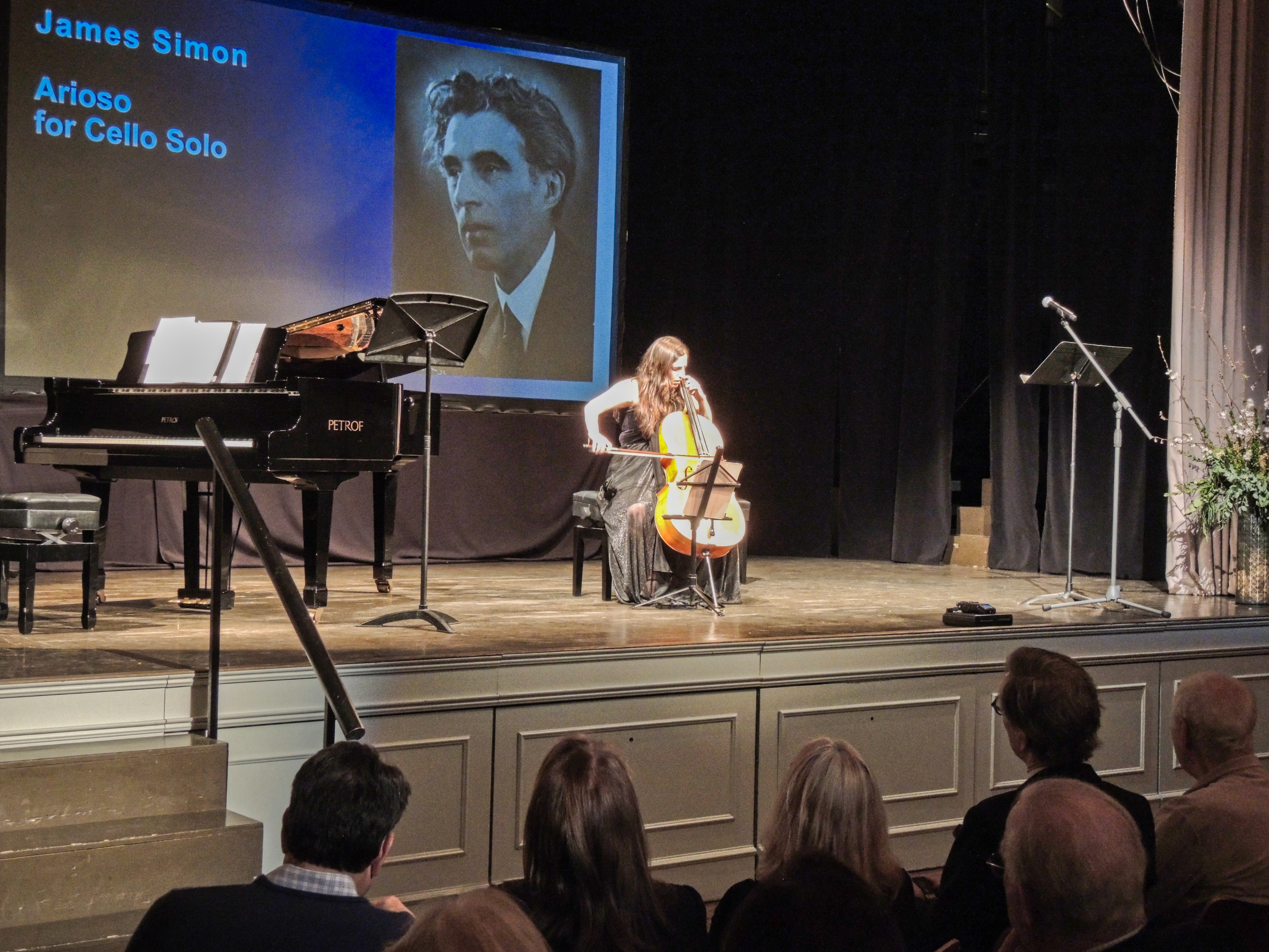 Tamar Sagiv performing James Simon's Arioso for cello solo beside a projected portrait of the composer